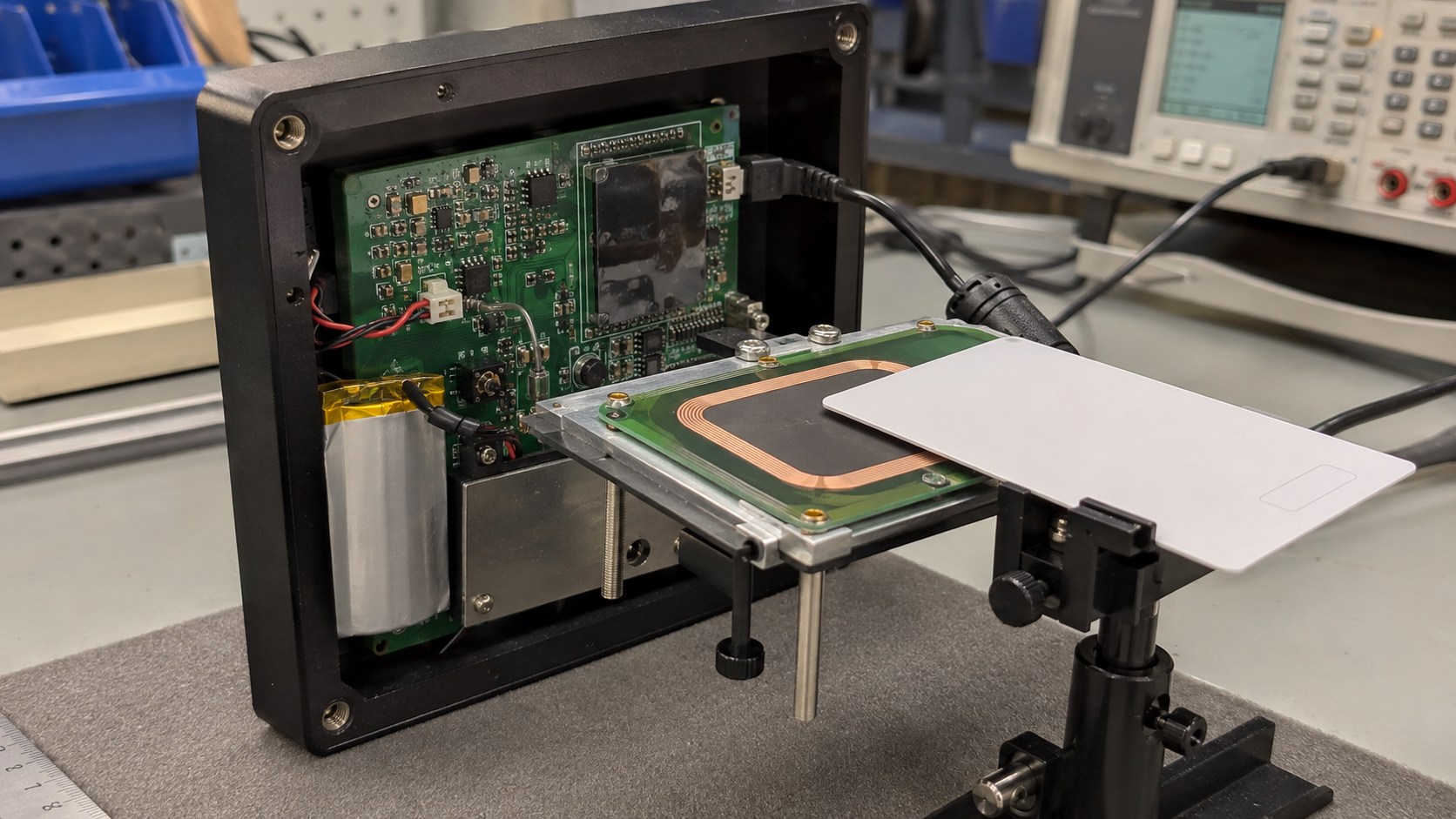 Open NFC reader enclosure with an antenna, ferrite, battery, target-card fixture and laboratory validation equipment